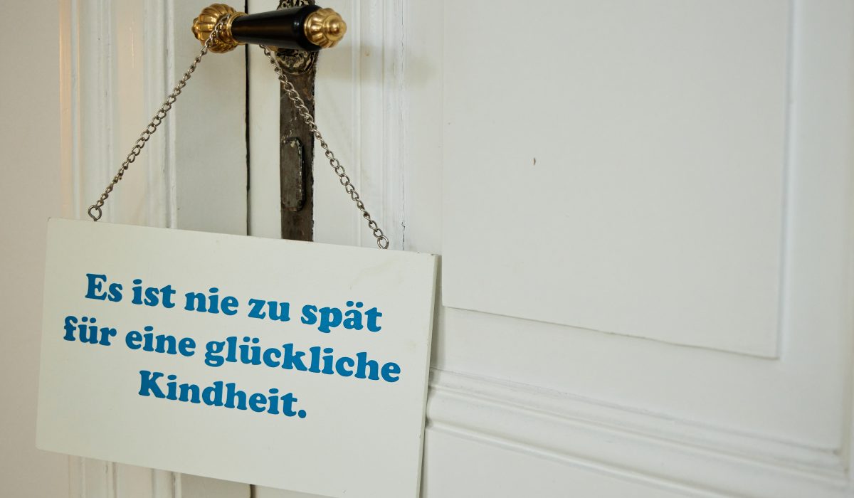 Schild an der Tür: Es ist nie zu spät für eine glückliche Kindheit.